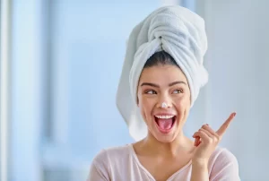 Smiling woman, her hair wrapped up in a towel, laughs at the tab of lotion on her nose